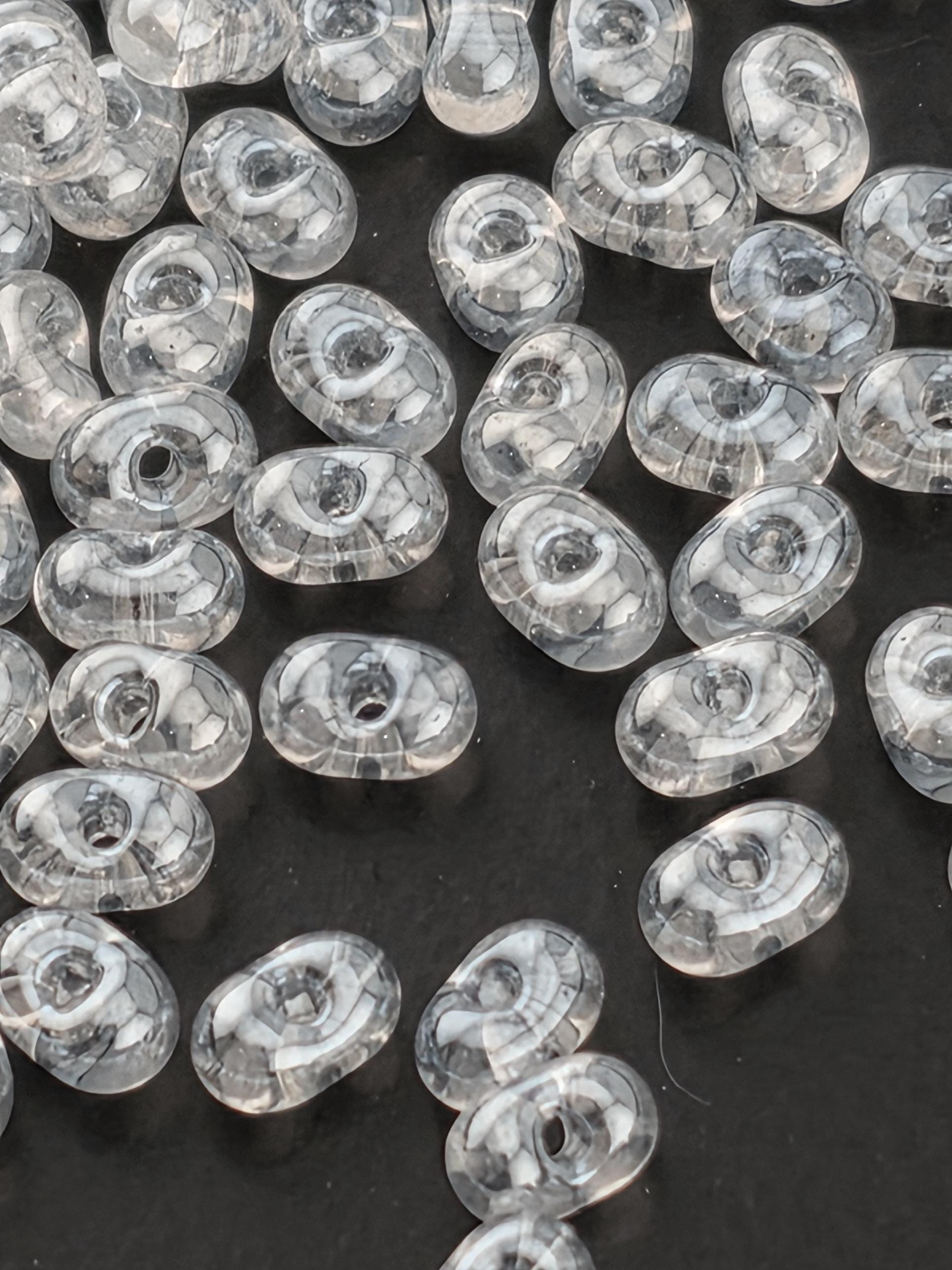 a collection of clear, oval-shaped glass beads scattered on a dark background.