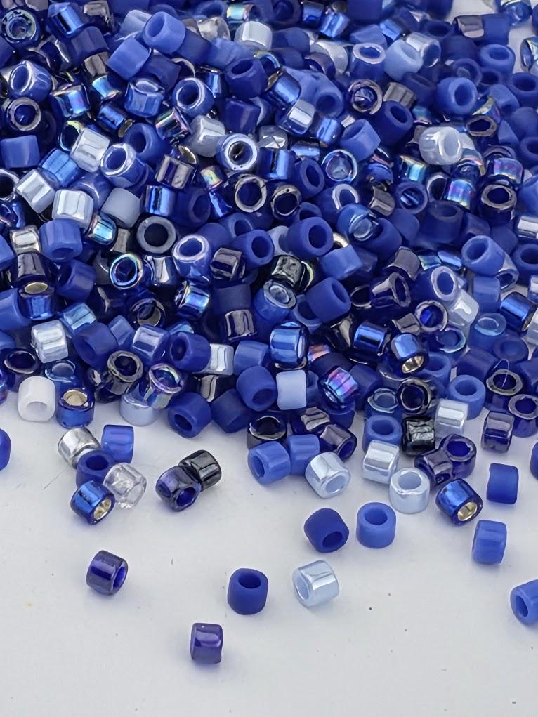 The image is a close-up of a pile of blue and silver beads scattered on a white surface.