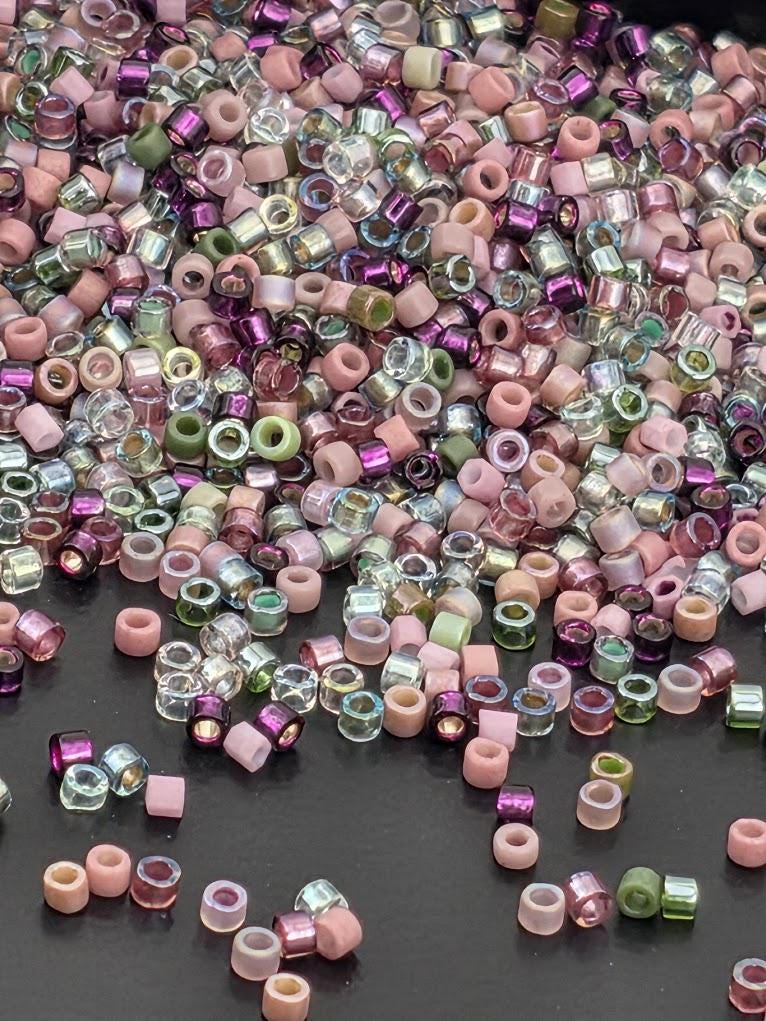 A large pile of multicolored beads, including clear and colored glass beads, scattered on a dark surface.