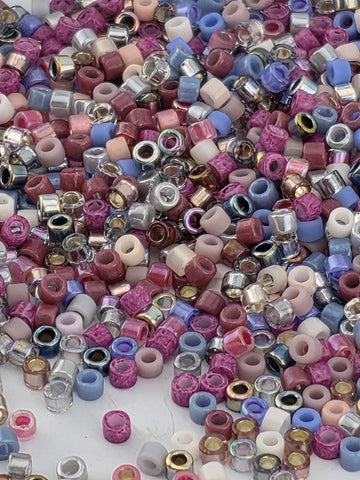 The image is a colorful assortment of various beads and small objects, including metallic and glass beads in shades of pink, purple, blue, and silver.