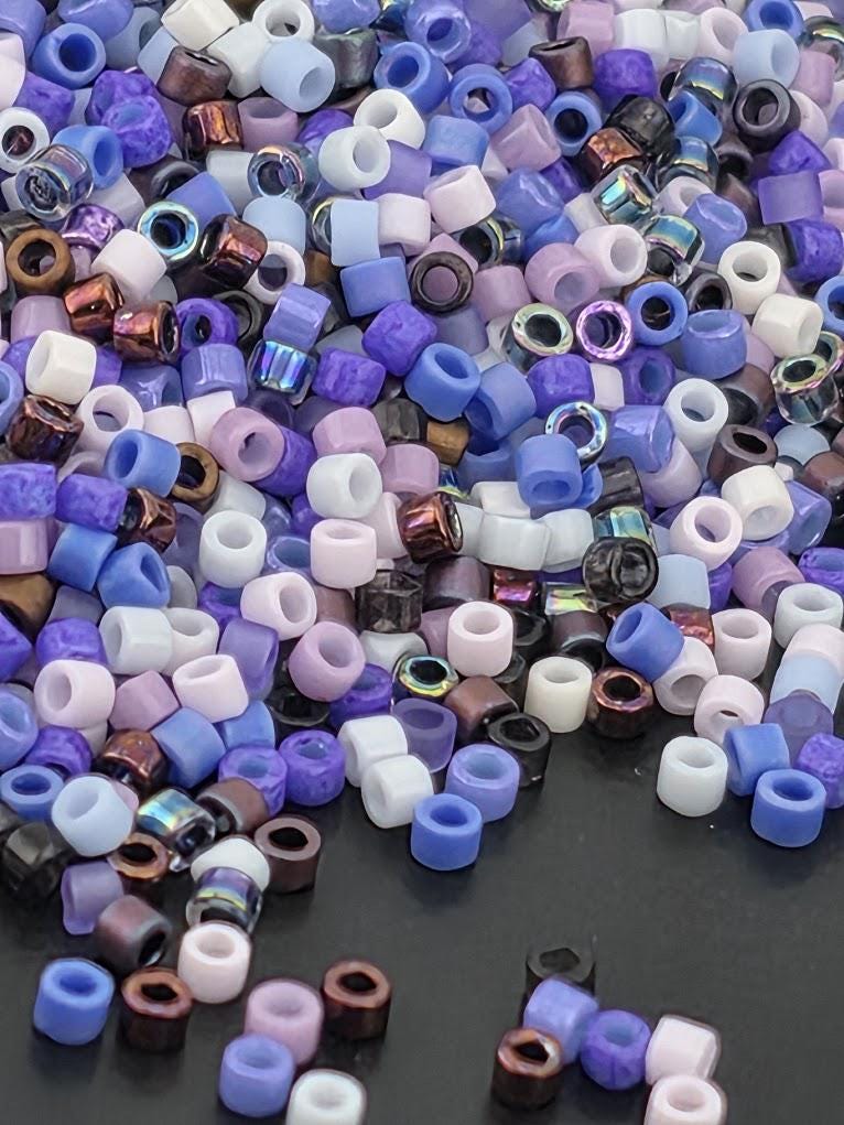 A colorful pile of multicolored beads, including white, purple, blue, and brown, scattered on a dark surface.