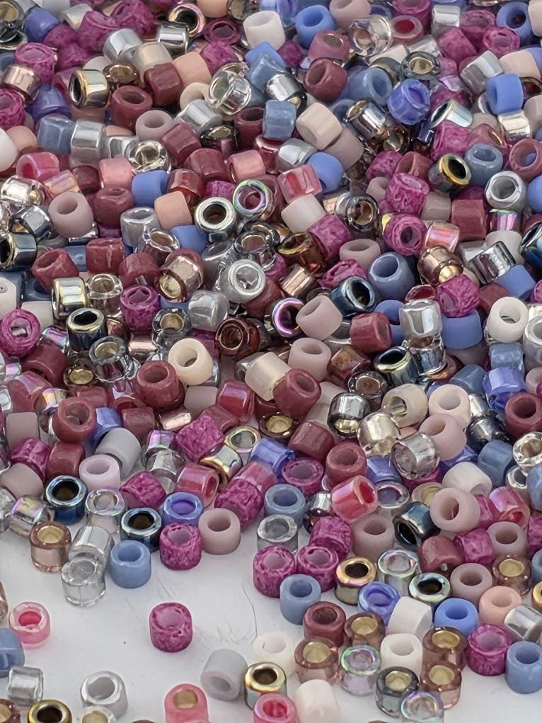The image is a colorful assortment of various beads and trinkets, including multicolored beads in shades of pink, purple, blue, and silver, as well as other small decorative items.
