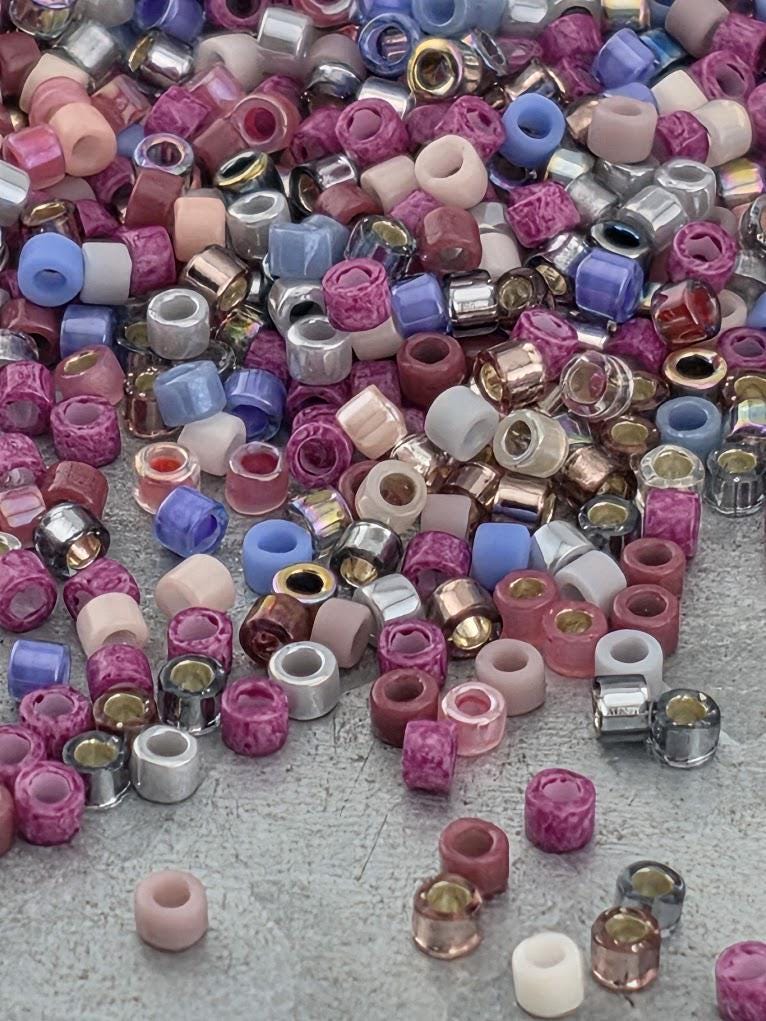 A colorful assortment of beads in various shapes and sizes, including metallic and multicolored beads, scattered on a surface.