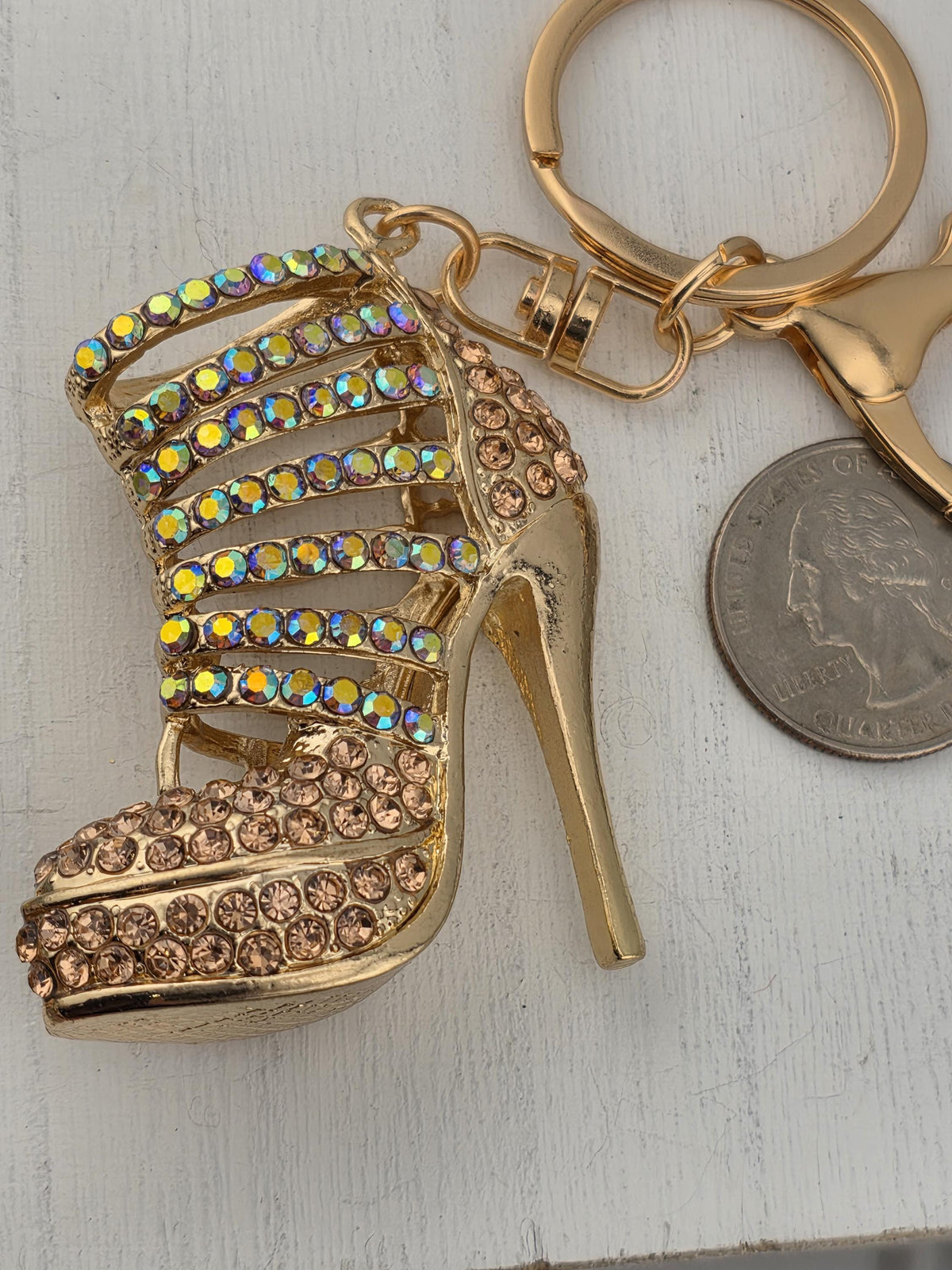 A gold-colored high-heeled shoe keychain with rhinestones and a coin keychain are placed on a white surface.