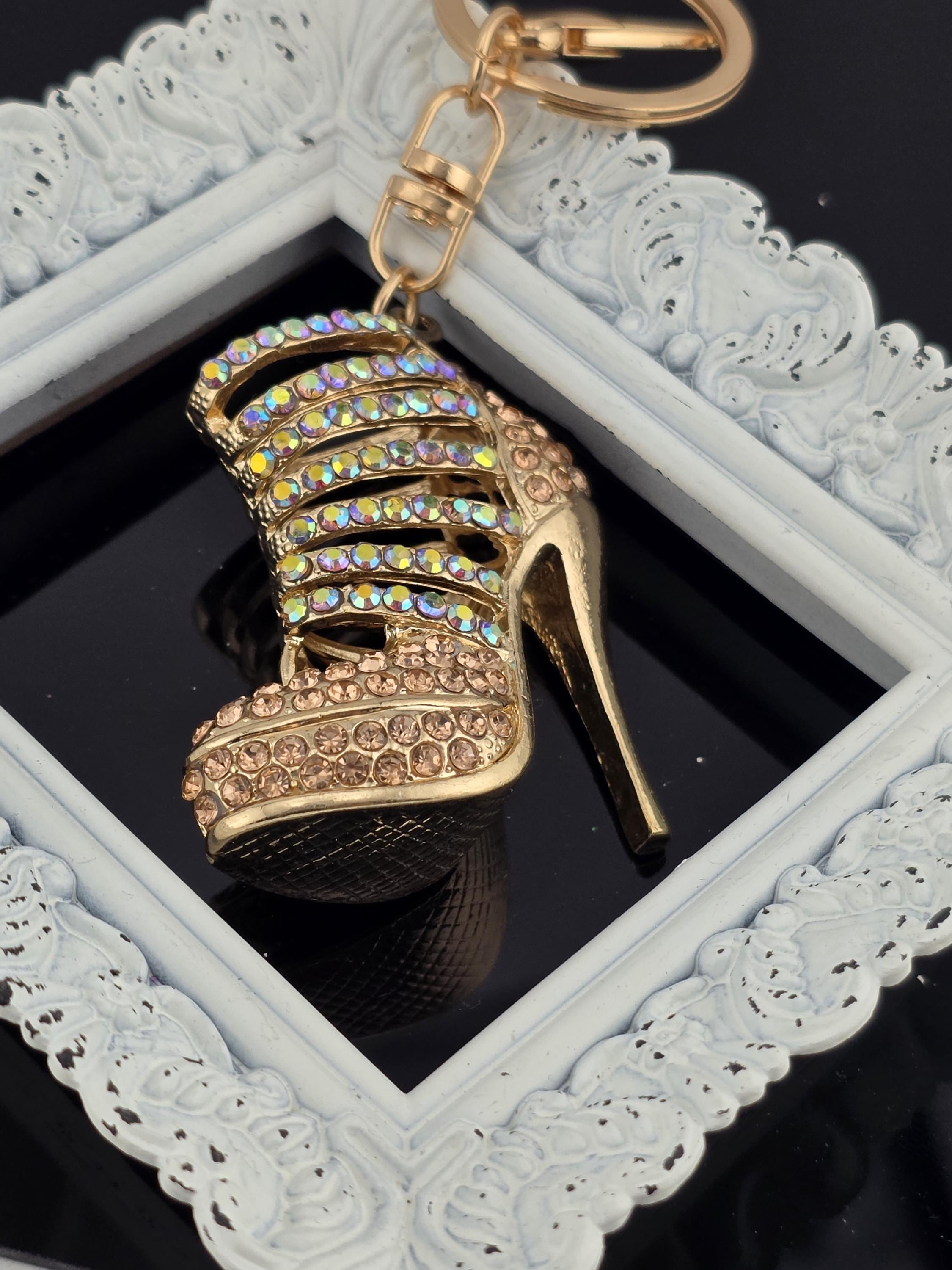 A decorative keychain with a gold-colored high-heeled shoe and rhinestone embellishments, displayed within a white ornate frame.