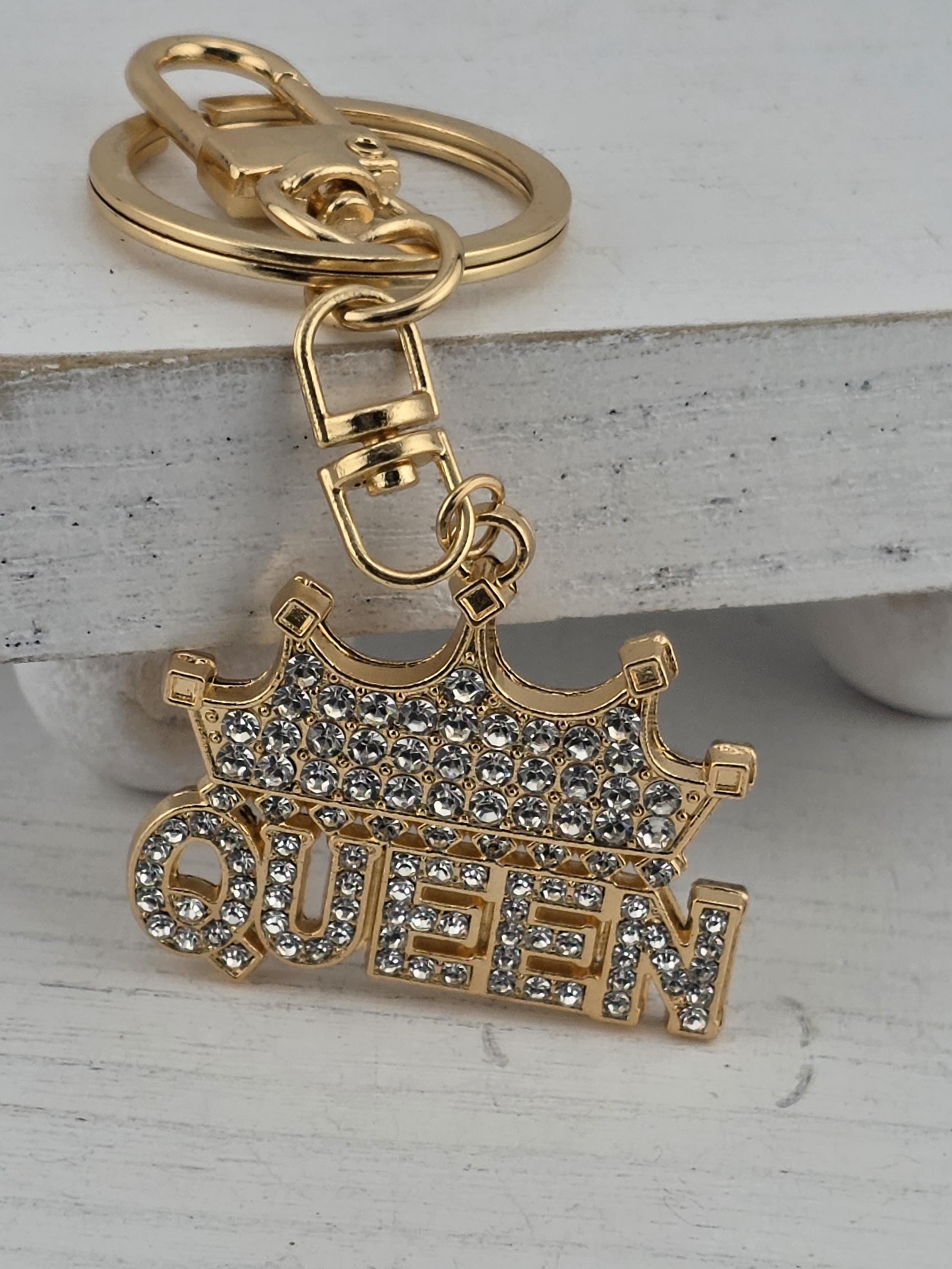 A gold-colored keychain with a crown-shaped charm and the word "QUEEN" written on it.
