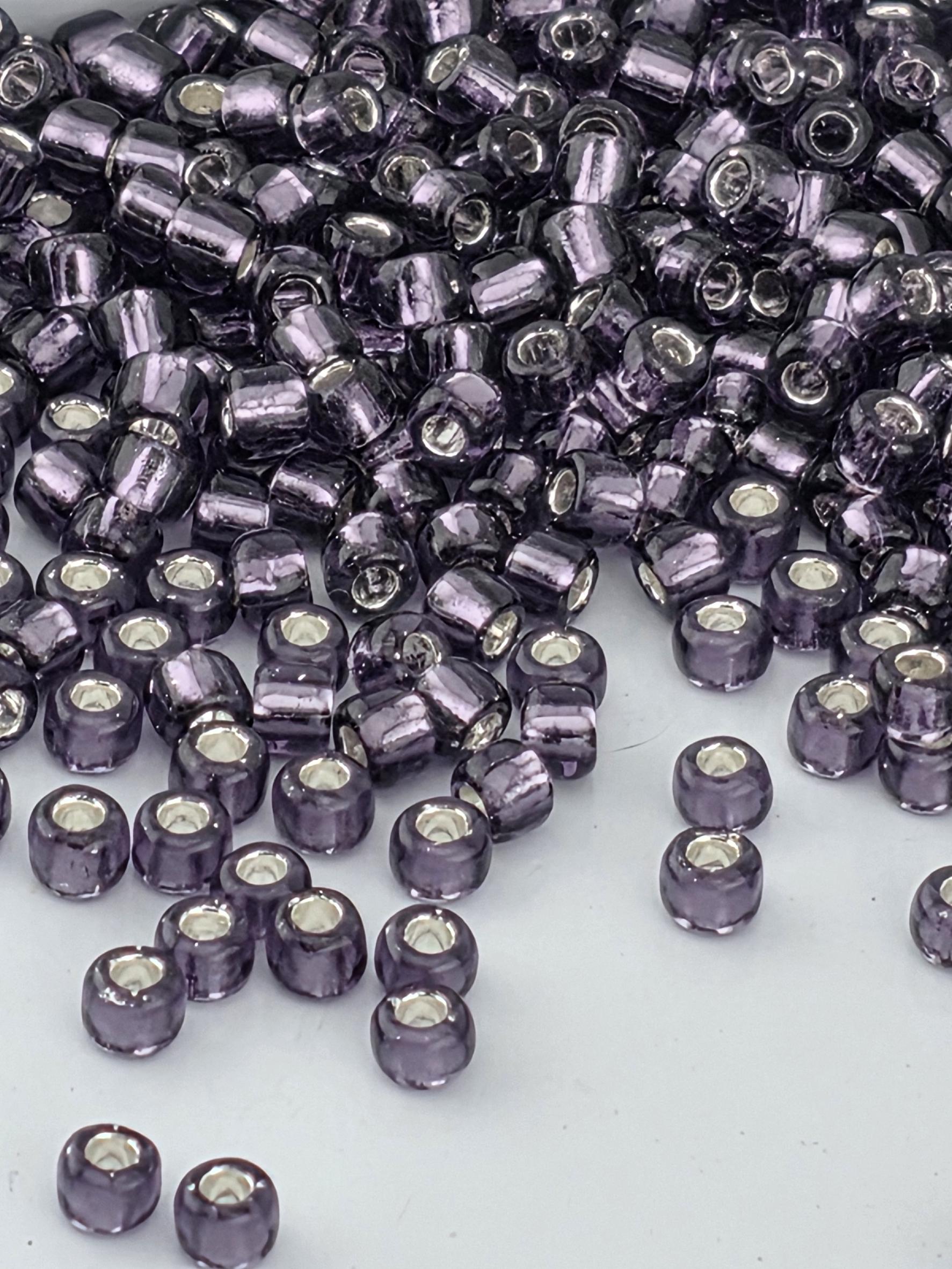 A close-up image of numerous purple glass beads scattered on a white surface.