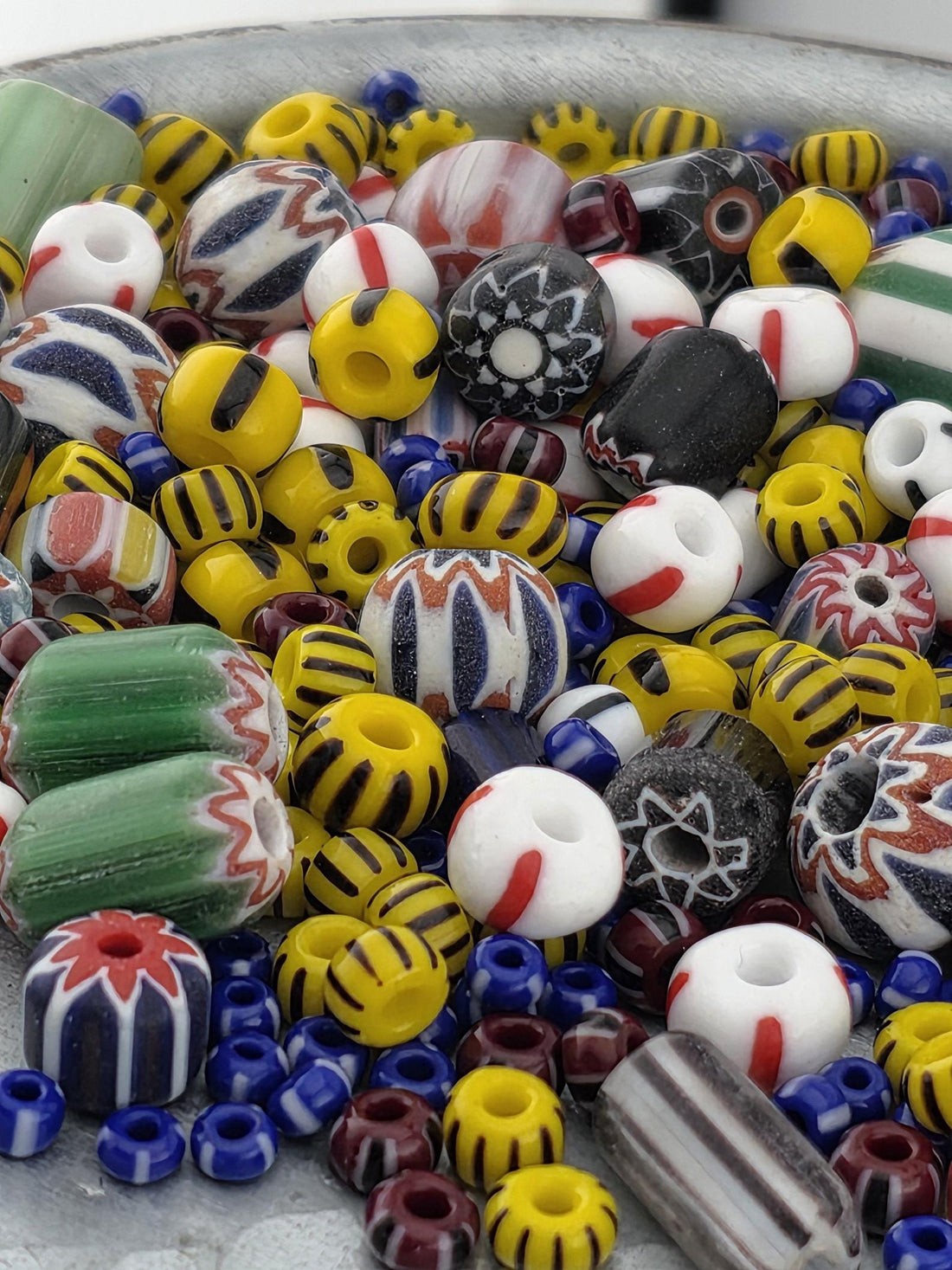 A colorful assortment of beads, including glass beads in various colors and patterns, is scattered across a surface.