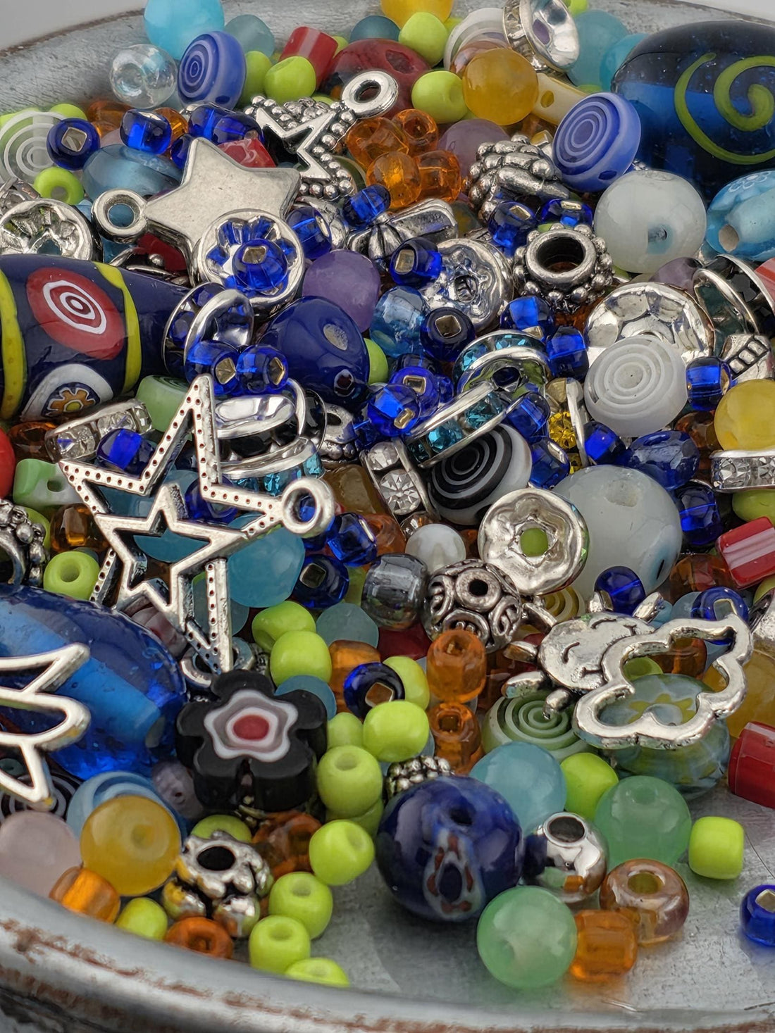 A colorful assortment of beads, charms, and other decorative items are scattered together in a bowl or container.
