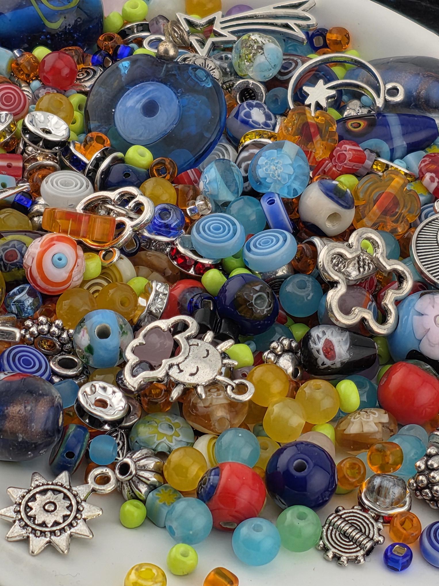 The image is a colorful assortment of various beads, charms, and other decorative items, including glass beads, metal charms, and other embellishments, all piled together.
