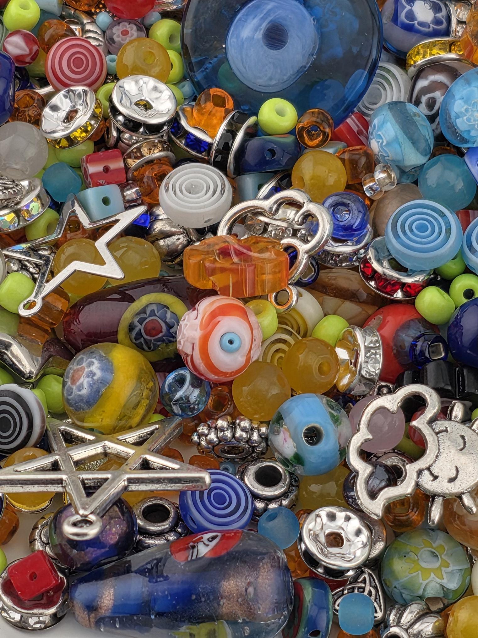 The image is a colorful assortment of various beads, charms, and other decorative items, including glass beads, metal charms, and star-shaped objects, all arranged in a visually appealing manner.