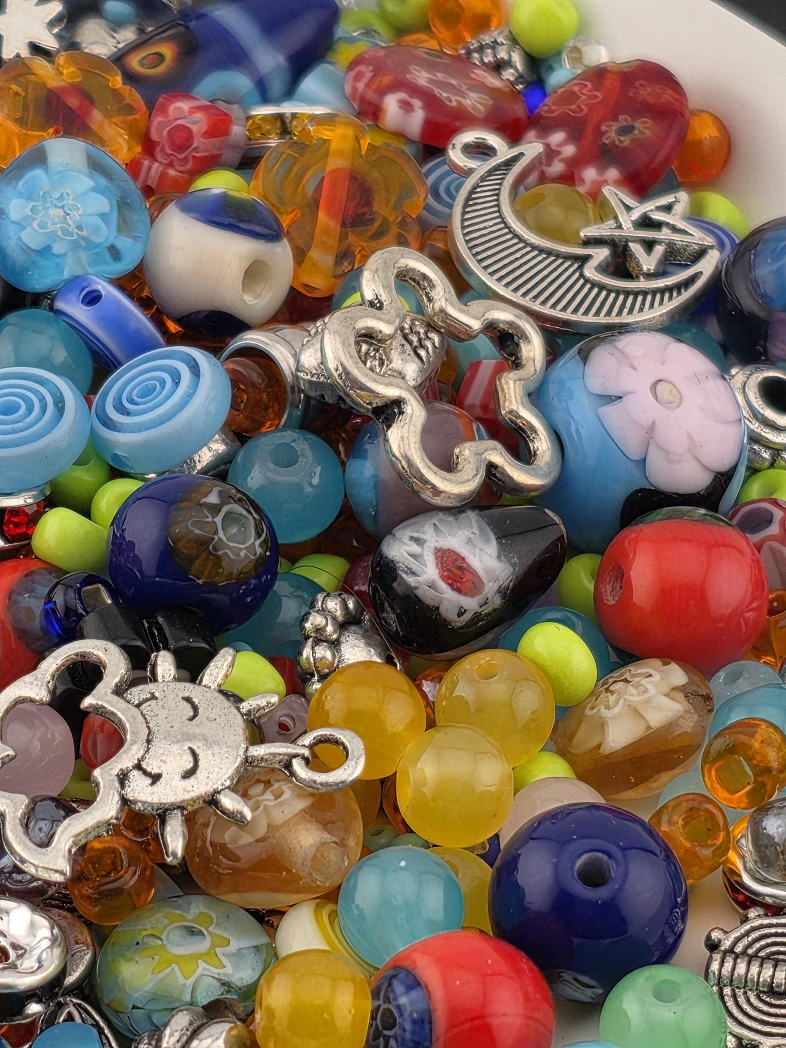 A colorful assortment of beads, charms, and other decorative items, including a crescent moon, flower, and star, creating a visually appealing and diverse collection.