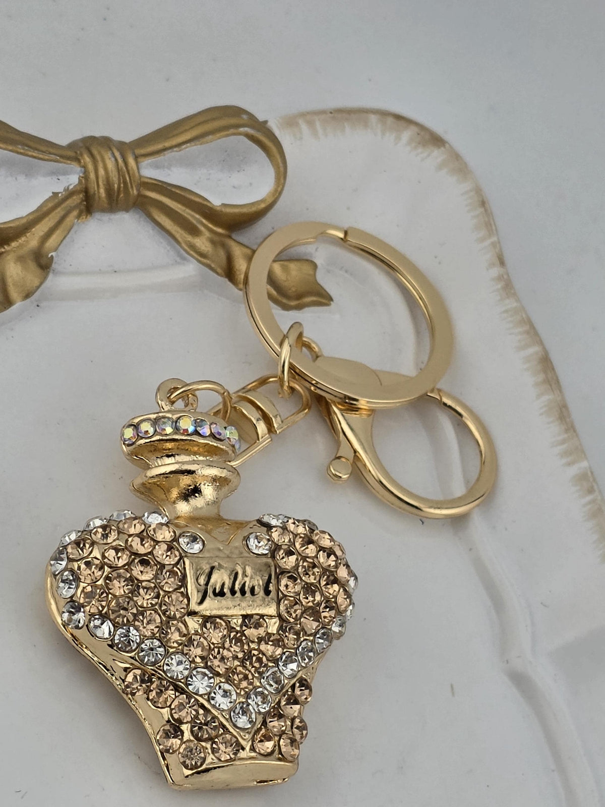 a gold-colored perfume bottle keychain with a bow and a keyring, all set against a white background.
