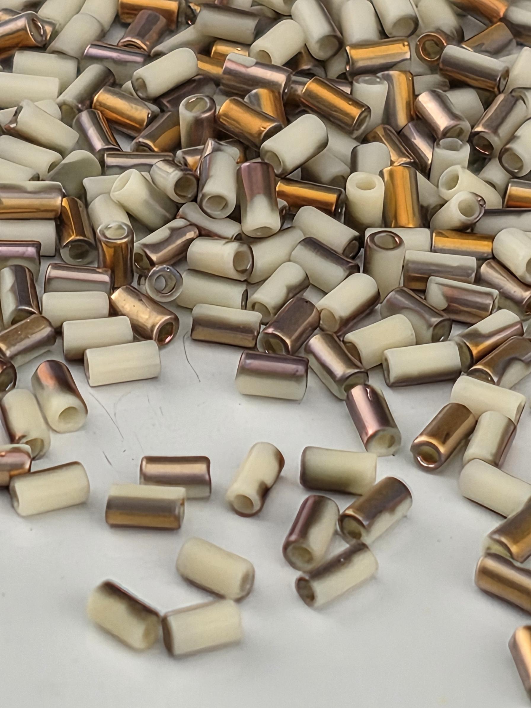 a collection of small, cylindrical objects with a mix of white, brown, and gold colors. The objects appear to be made of metal and are scattered across a white surface.