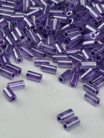 a close-up view of numerous small, clear beads in various shades of purple, scattered across a white surface.