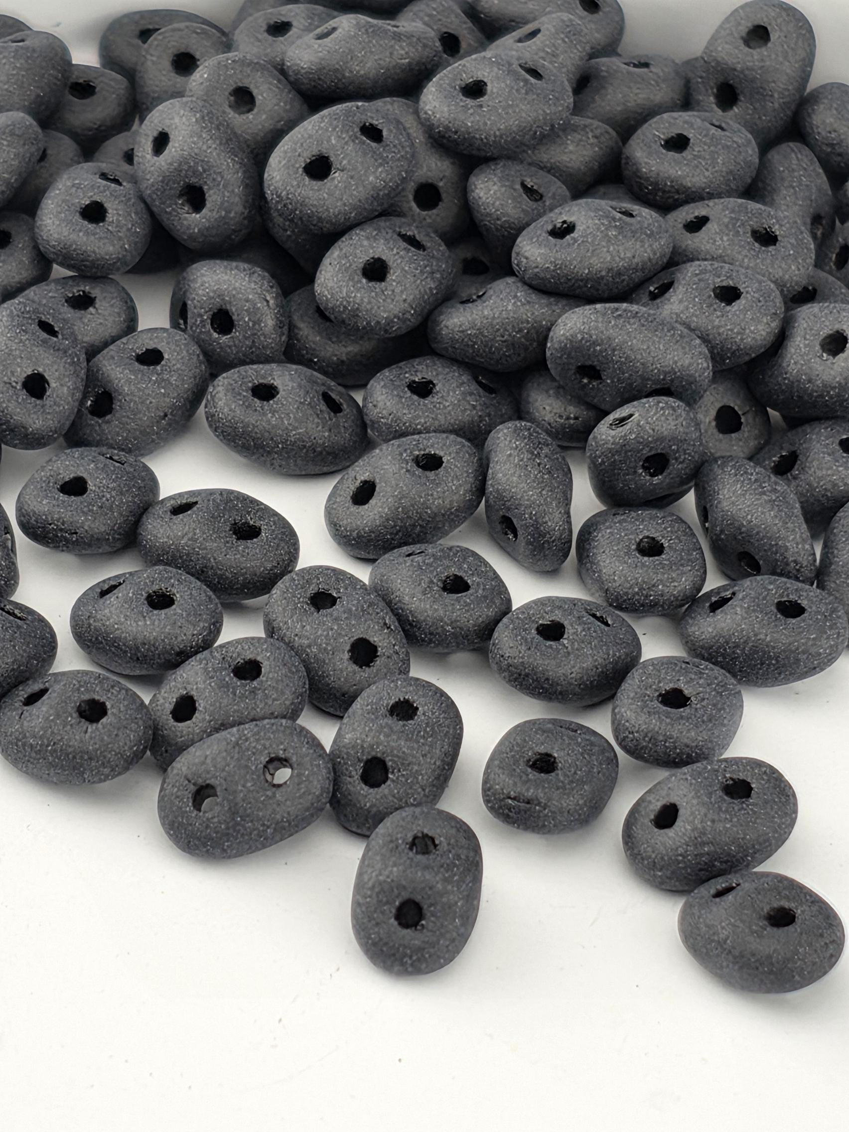a pile of small, black beads or stones with holes scattered across a white background.