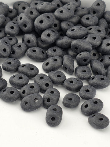 a pile of small, black beads or stones with holes scattered across a white background.