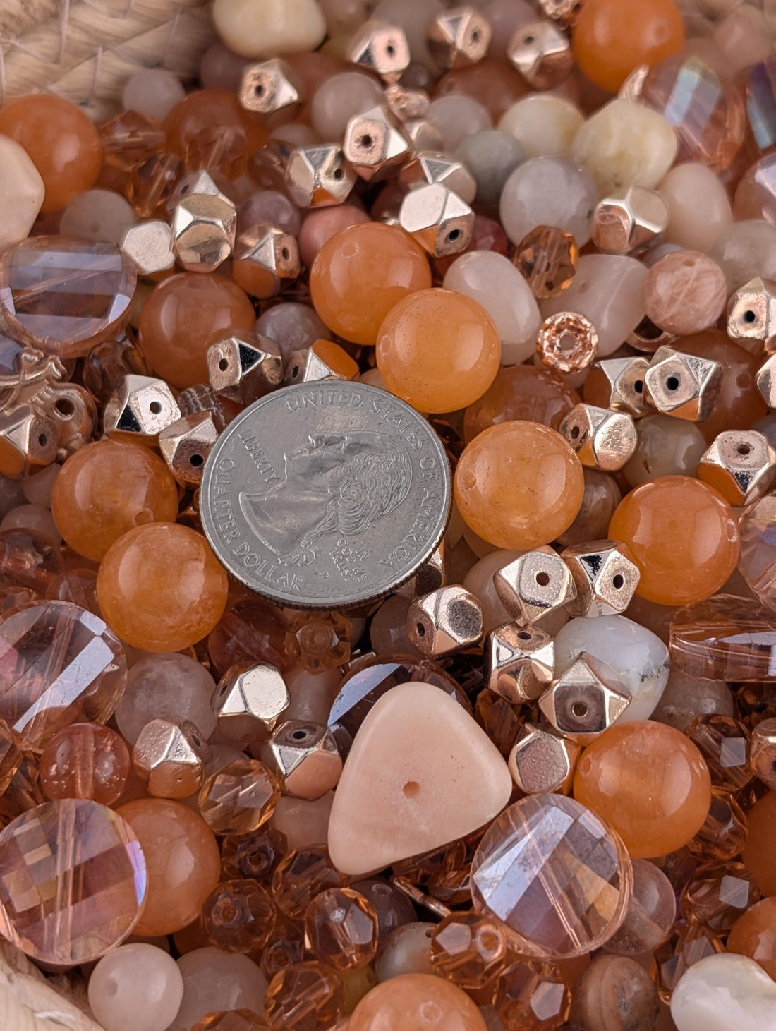 The image is a close-up of various beads and gemstones, including white, orange, and pink stones, as well as some with metallic accents.
