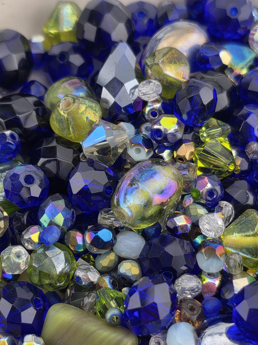 The image is a close-up of a collection of colorful glass beads, including blue, green, yellow, and silver beads, arranged in a visually appealing manner.