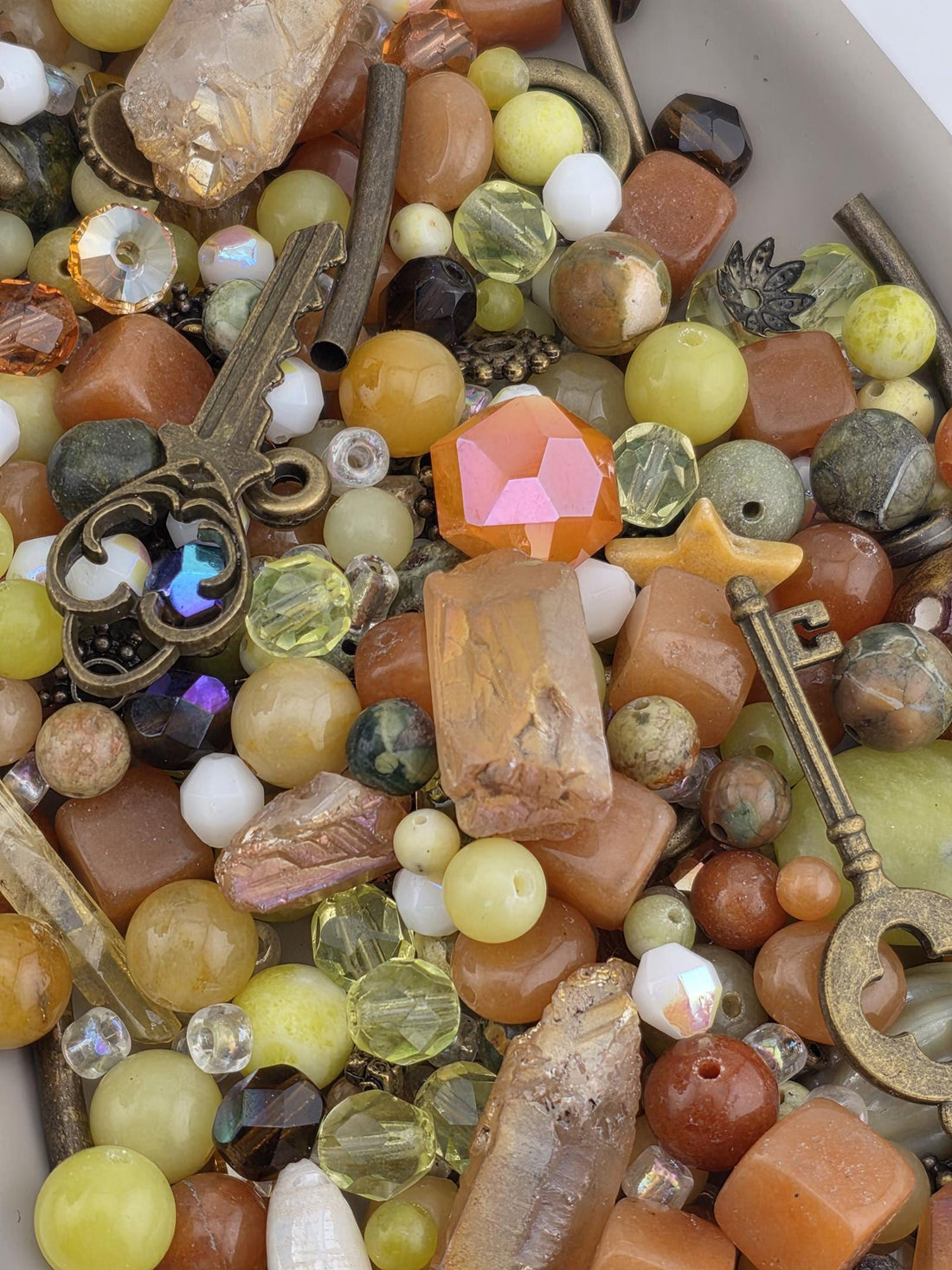 The image is a close-up of a collection of various colorful beads, gemstones, and metal objects, including a key, scattered together.