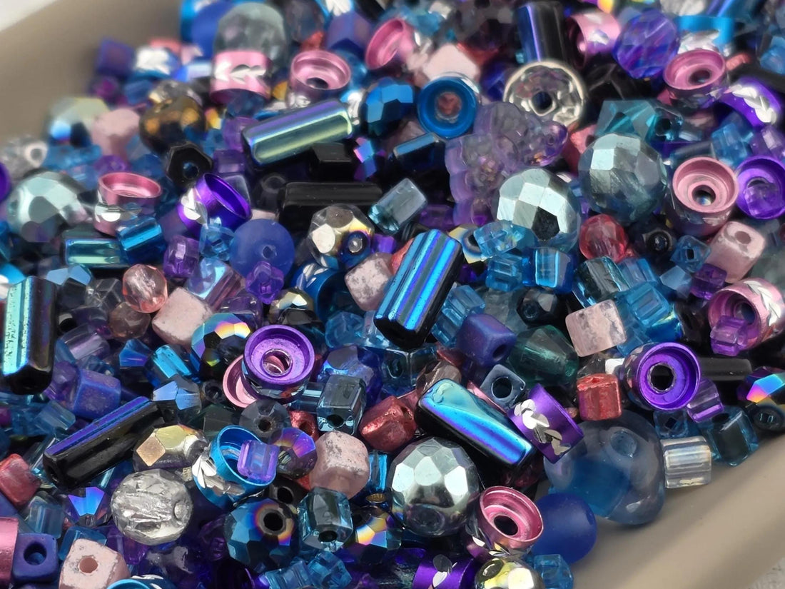 A close-up image of a pile of colorful beads, including various shapes and sizes, such as glass, metal, and plastic beads, scattered together.