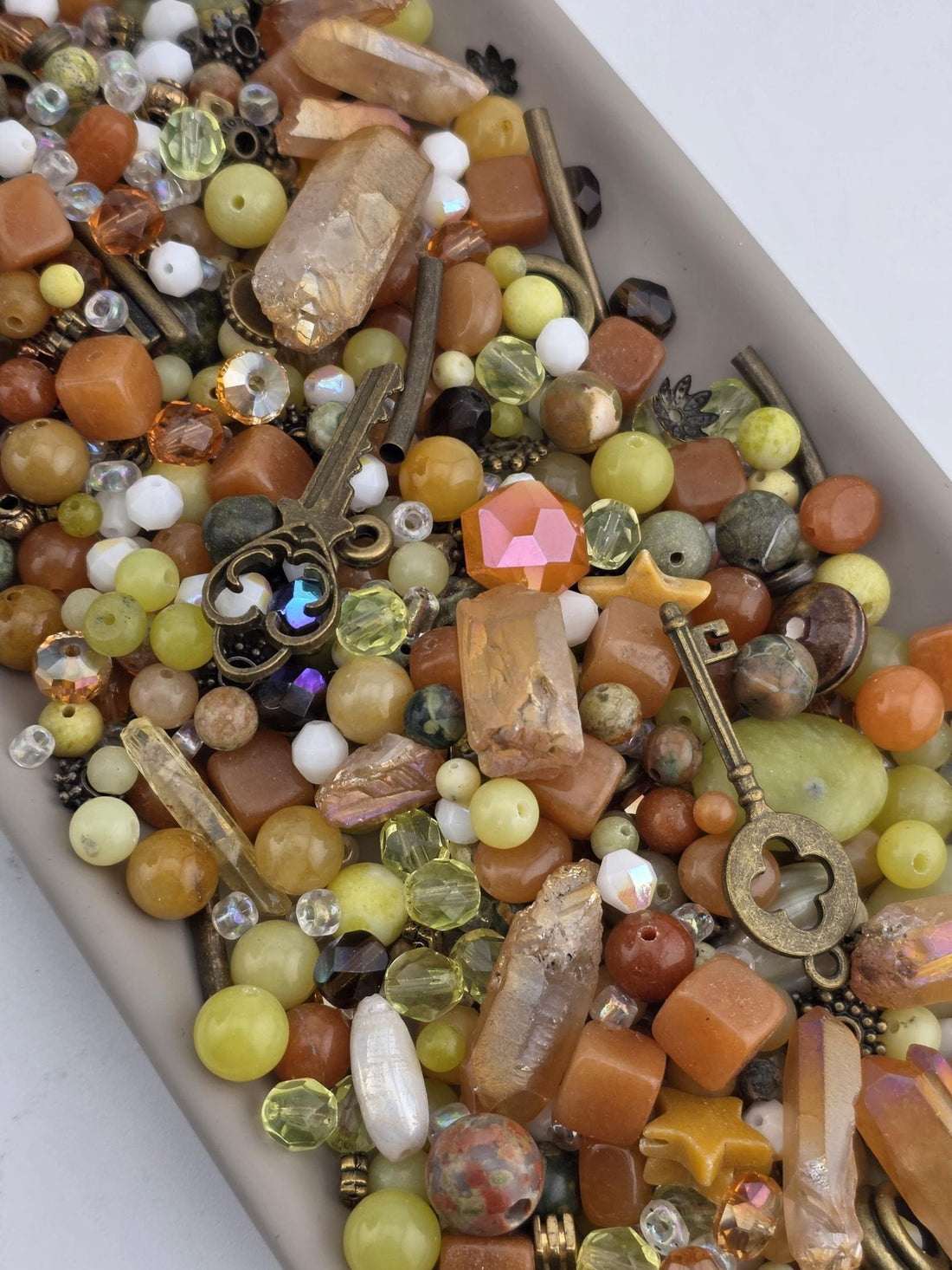 The image is a close-up of a collection of various colorful beads, gemstones, and metal objects, including a key, scattered together.