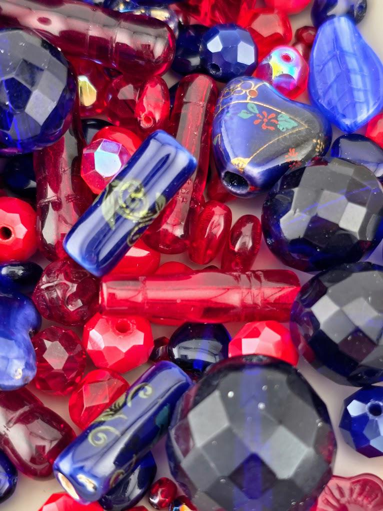 The image is a close-up of various colorful beads, including red, blue, and multicolored beads, scattered together.