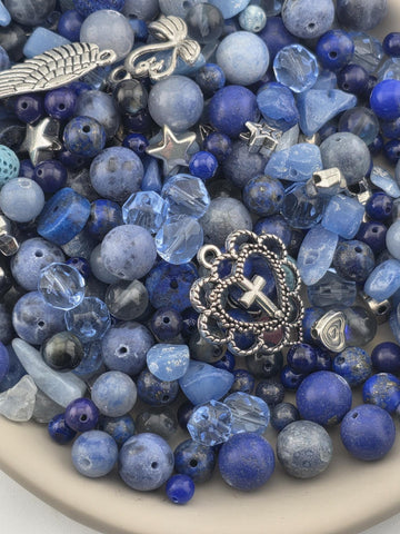 A bowl filled with various blue beads, charms, and other decorative items.