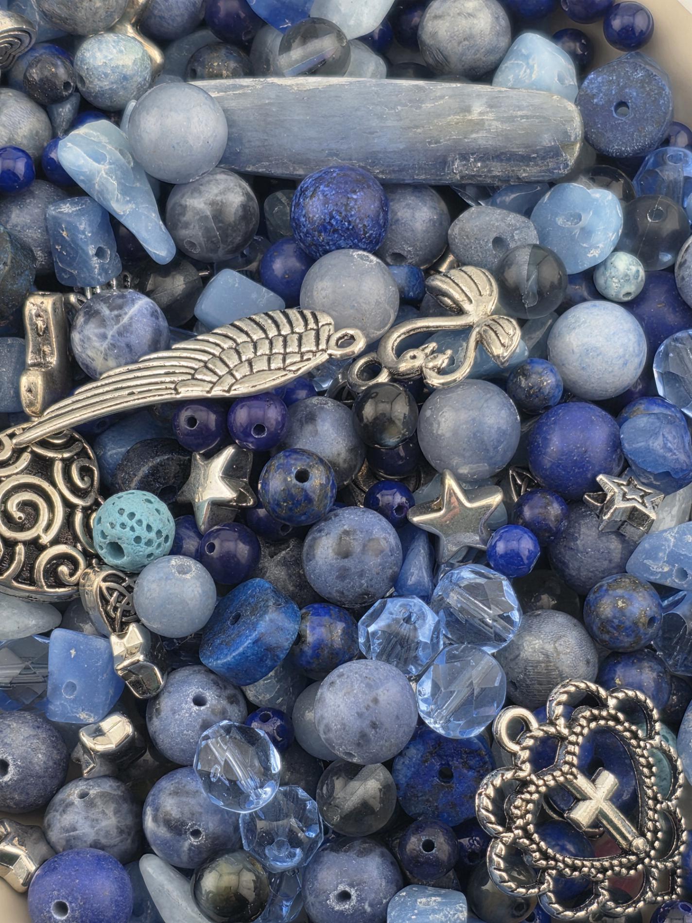 The image is a close-up of various blue beads, charms, and other blue-colored objects, including a silver cross.