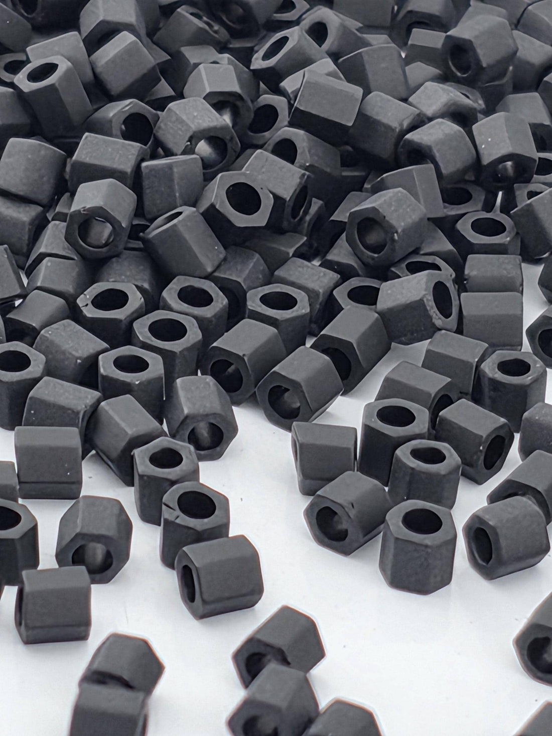 a large pile of black hexagonal nuts or bolts scattered across a white surface.