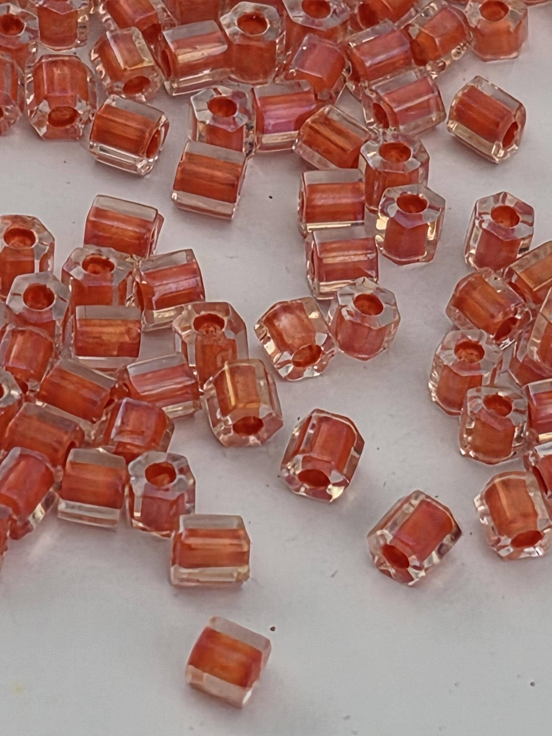 a collection of small, clear, hexagonal-shaped objects in shades of orange and red, scattered across a white surface.