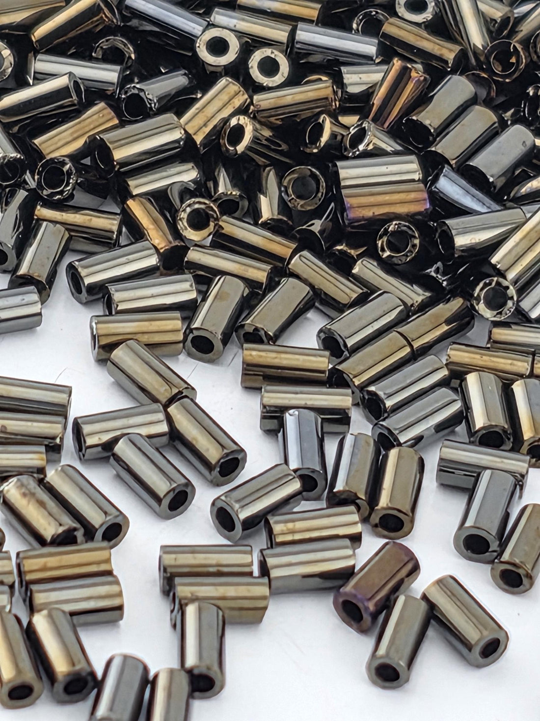 a collection of various metal rods and tubes, with a mix of metallic colors including silver, black, and gold. The rods appear to be made of a shiny, metallic material and are scattered across a surface.