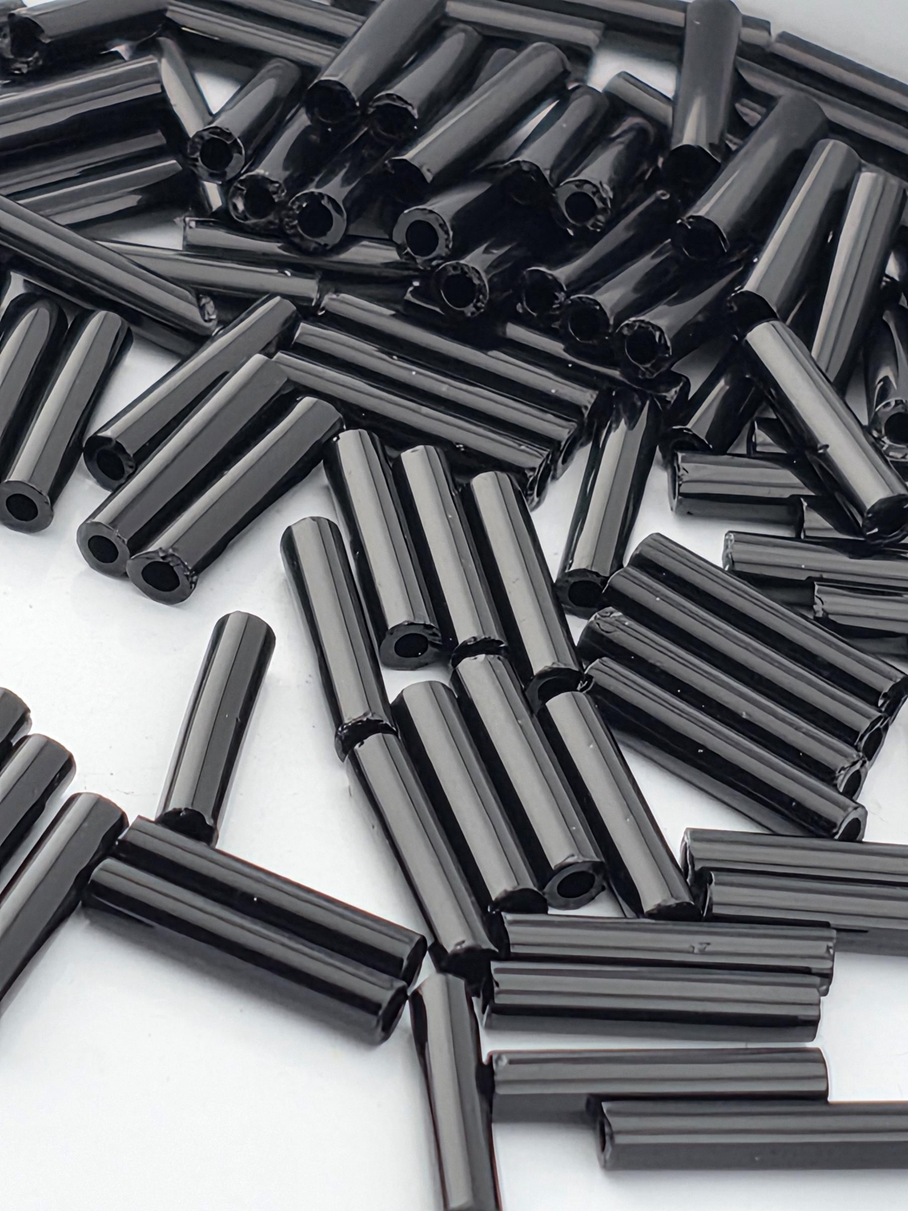 numerous black cylindrical objects, possibly beads or tubes, scattered across a white background.