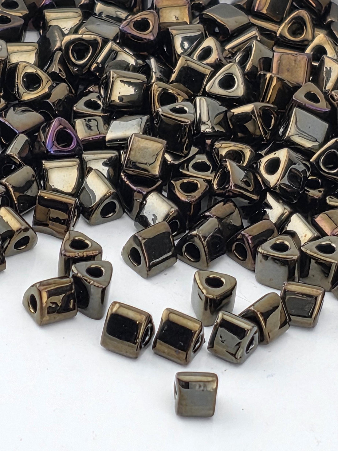 a pile of small, square-shaped metal beads in various shades of black and brown, scattered on a white surface.