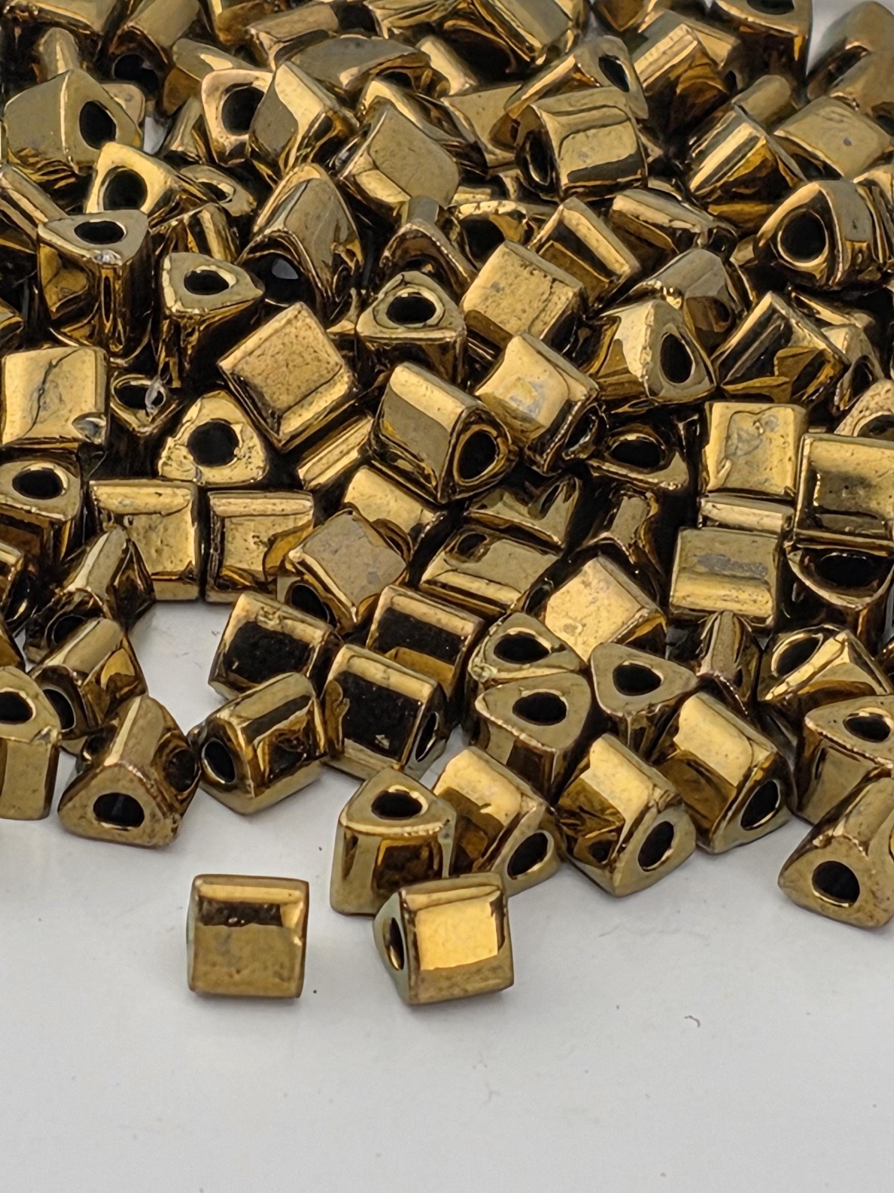 a pile of small, square-shaped, shiny gold-colored beads or beads with a metallic appearance.