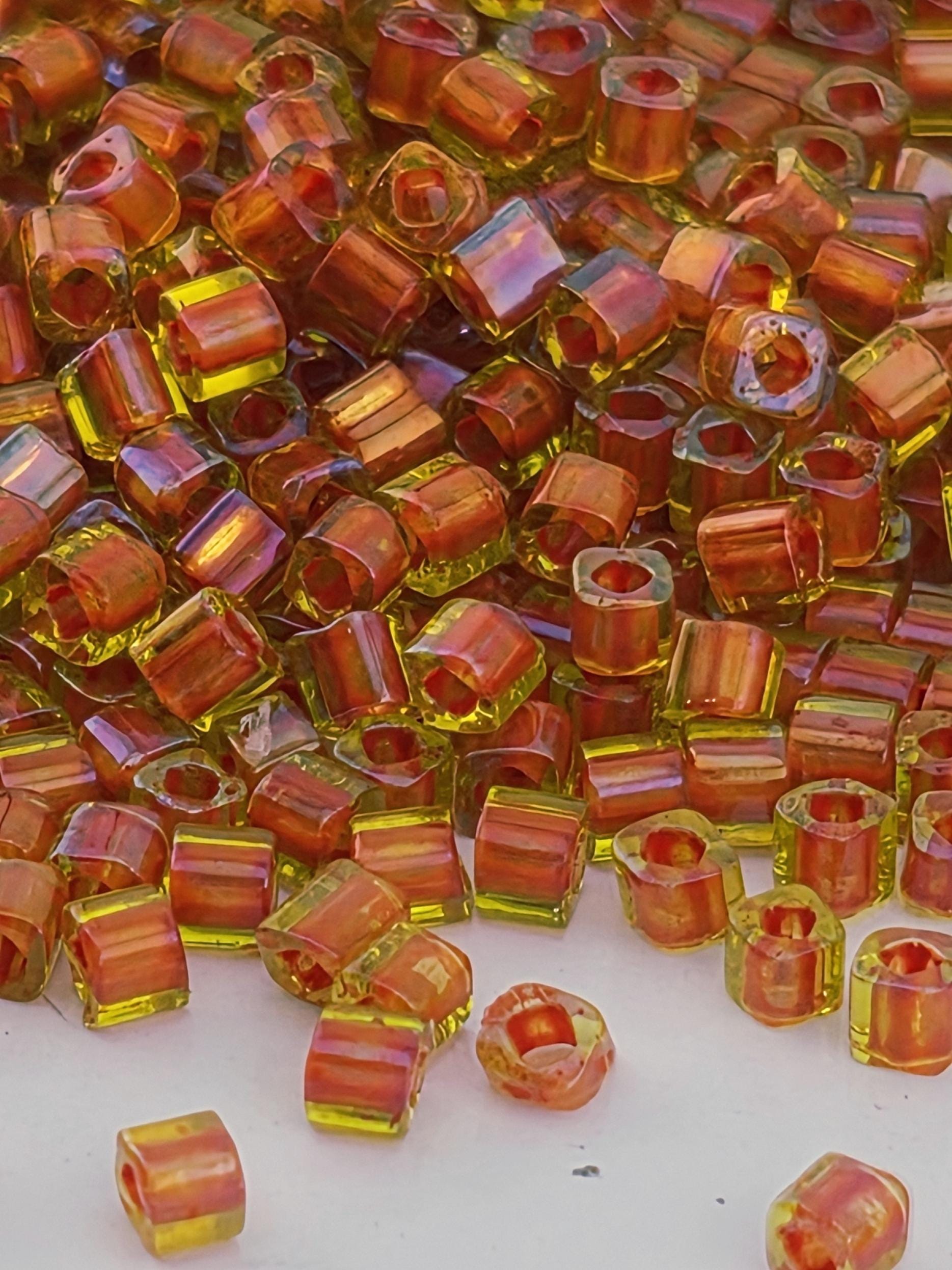 The image is a close-up of numerous small, colorful beads in shades of orange and yellow, scattered across a surface.
