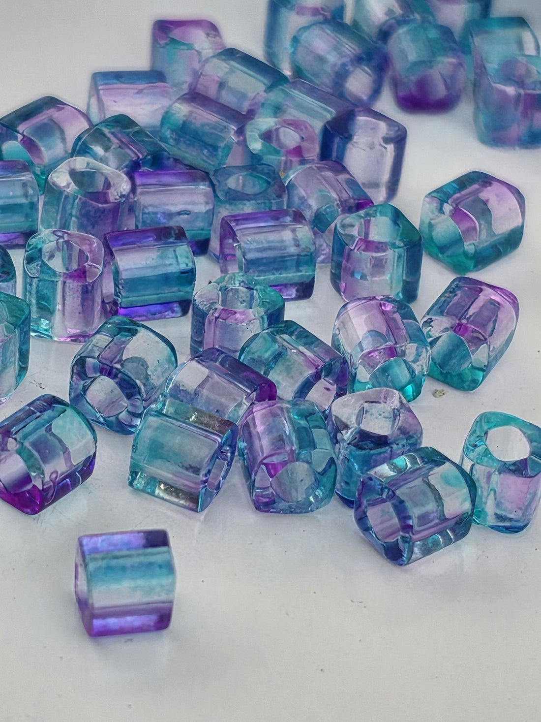 a collection of small, clear glass beads in various shades of blue and purple, scattered on a white surface.