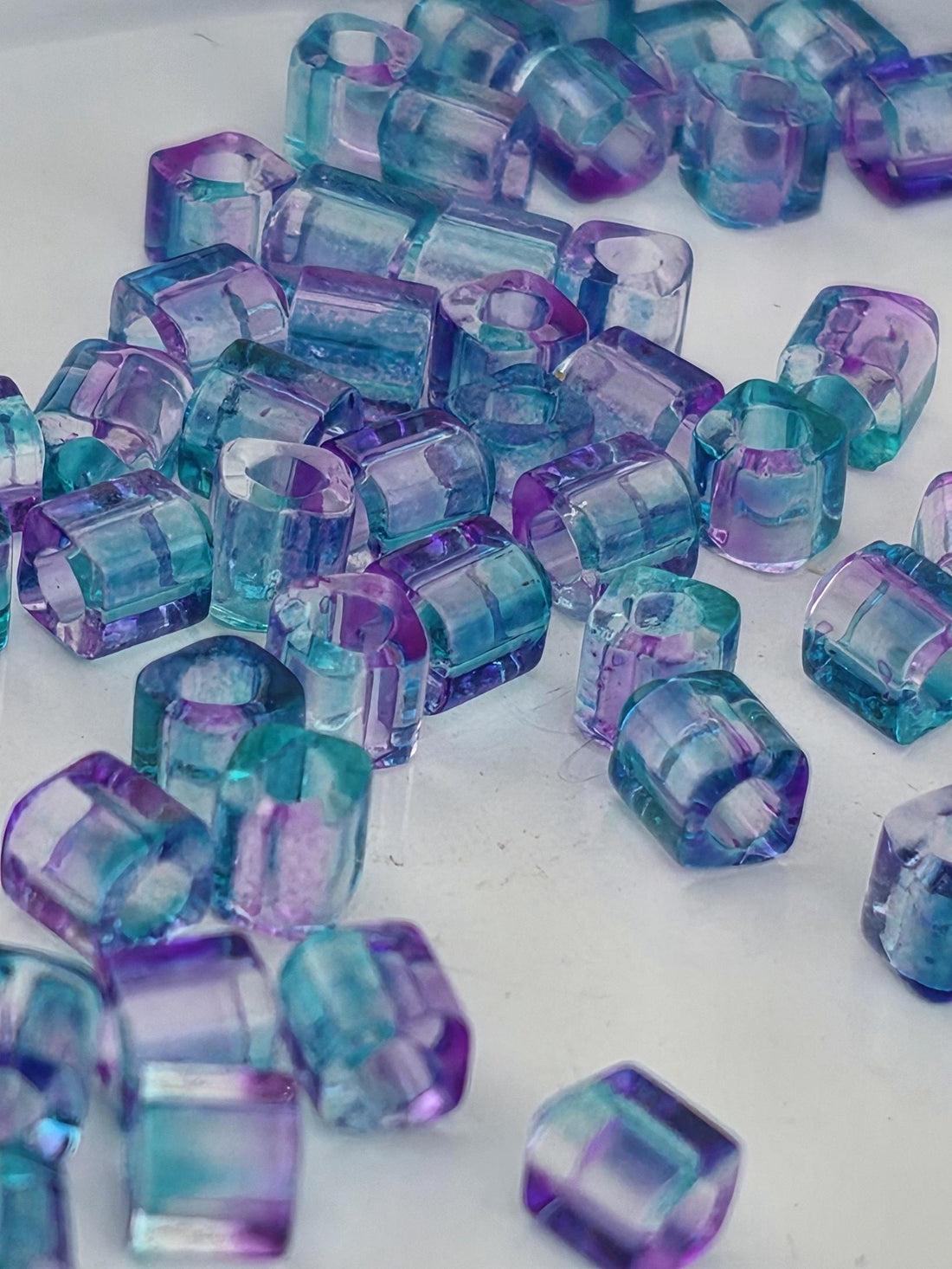 a collection of small, clear glass beads in various shades of blue and purple, scattered on a white surface.