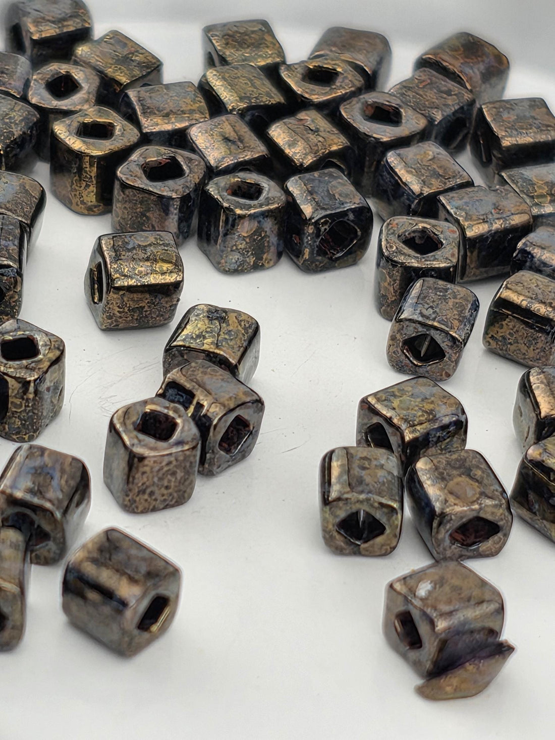 a collection of small, square-shaped metal objects with a dark, textured appearance, scattered on a white surface.