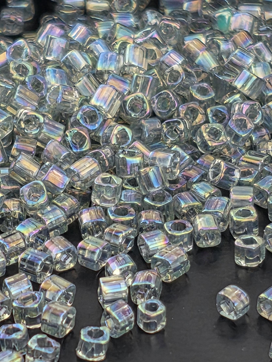 The image is a close-up of numerous clear, transparent beads scattered across a dark background.