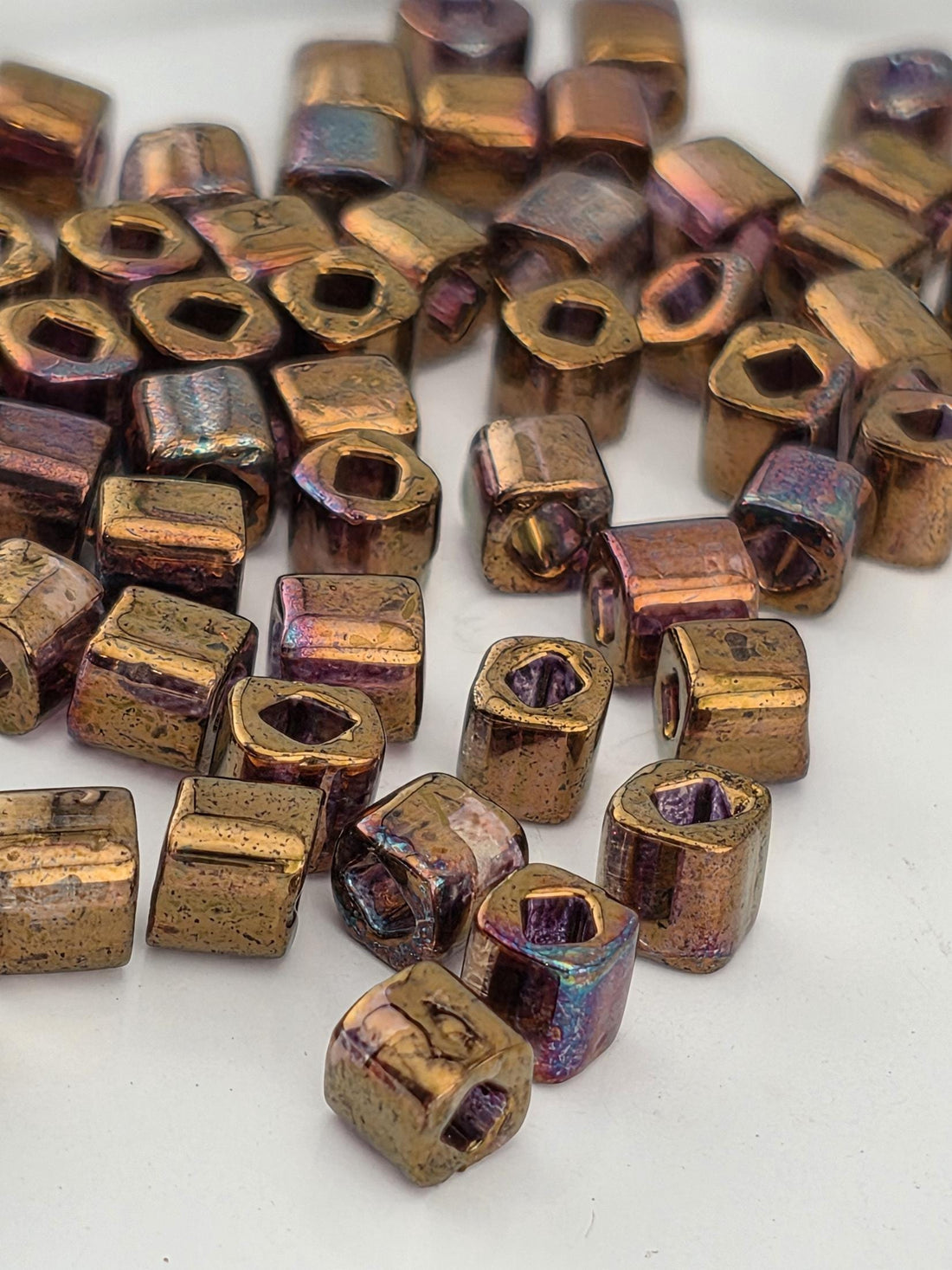 a collection of small, irregularly shaped metal beads in various colors, including gold, purple, and blue, scattered on a white surface.