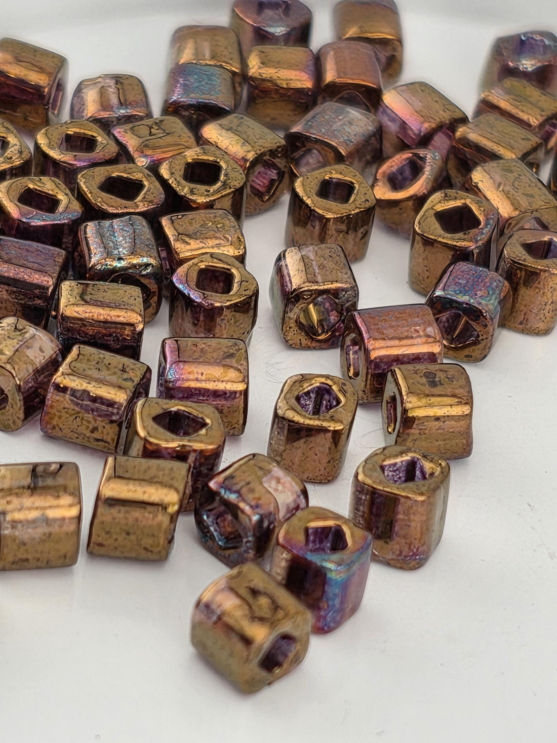 a collection of small, irregularly shaped metal beads in various colors, including gold, purple, and blue, scattered on a white surface.