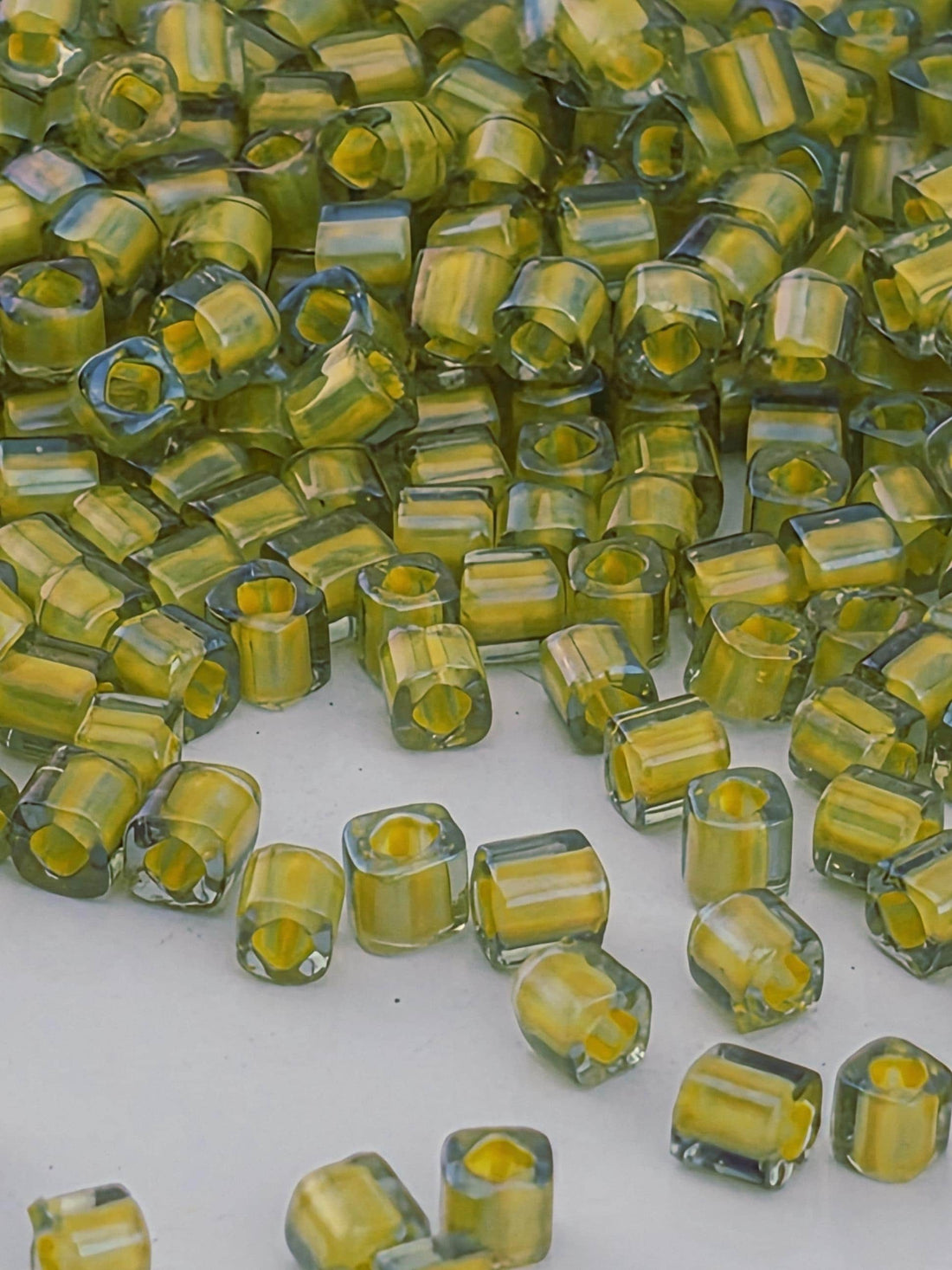 a close-up view of numerous small, clear glass beads in various shades of yellow and green, scattered across a white surface.