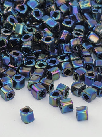 a collection of small, square-shaped metal beads in various colors, including blue, purple, and green, scattered on a white surface.