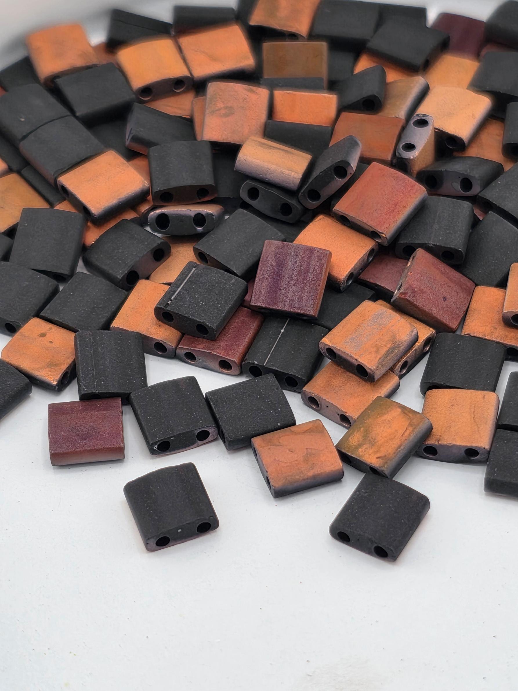 A pile of small, square-shaped objects in various colors, including black, orange, and brown, scattered on a white surface.