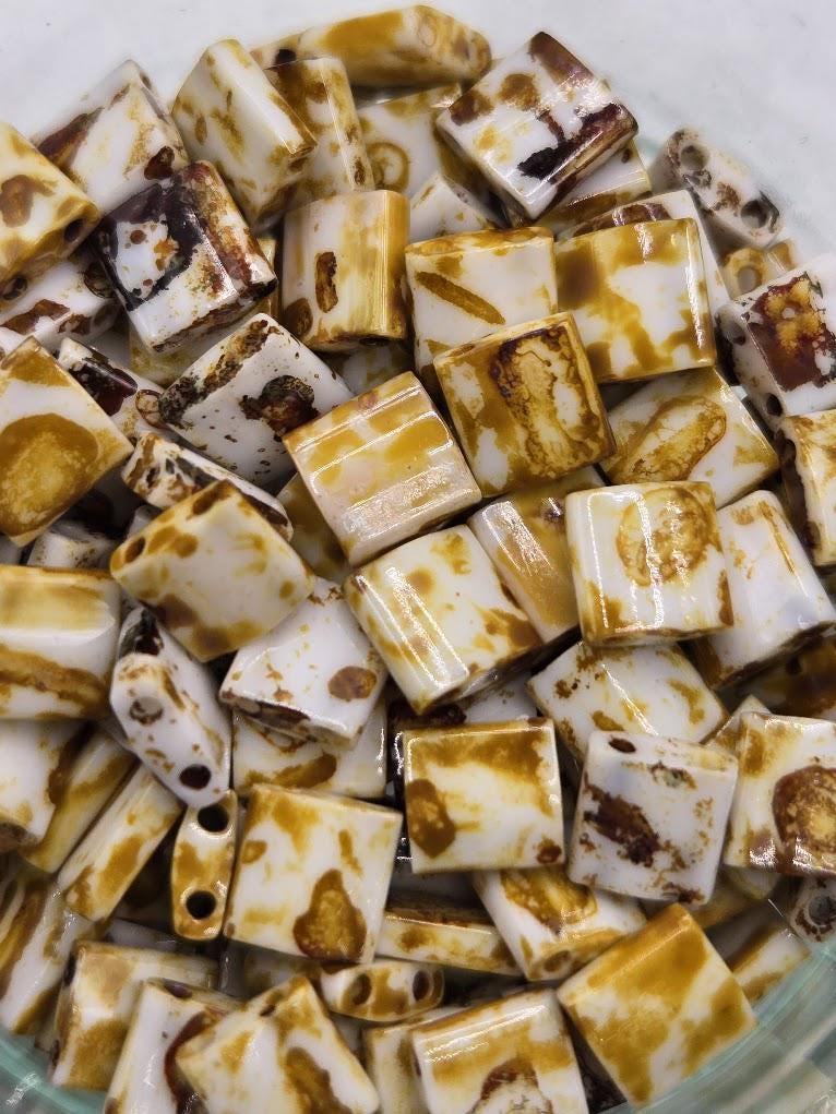 a close-up view of a pile of small, square-shaped objects with a yellow and brown color pattern. The objects appear to be made of a material that resembles wood or stone, and they are scattered across the frame, creating a visually interesting composition.