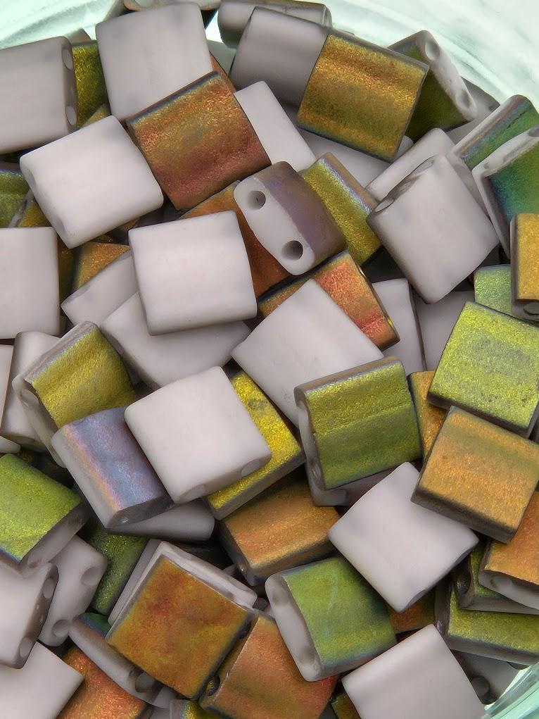 The image is a close-up of a pile of colorful, square-shaped beads in various shades of green, white, and orange.
