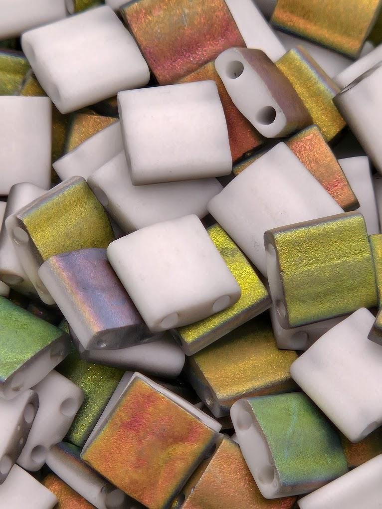 The image is a close-up of various colored glass beads, including white, green, and orange, arranged in a pile.