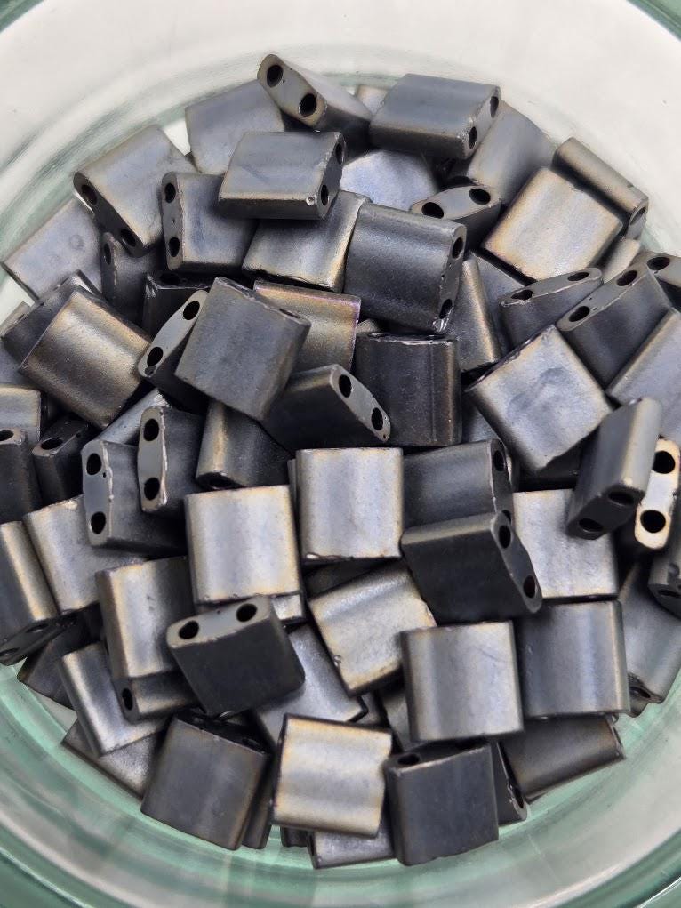 A glass bowl filled with numerous small, square-shaped metal pieces in various shades of gray.