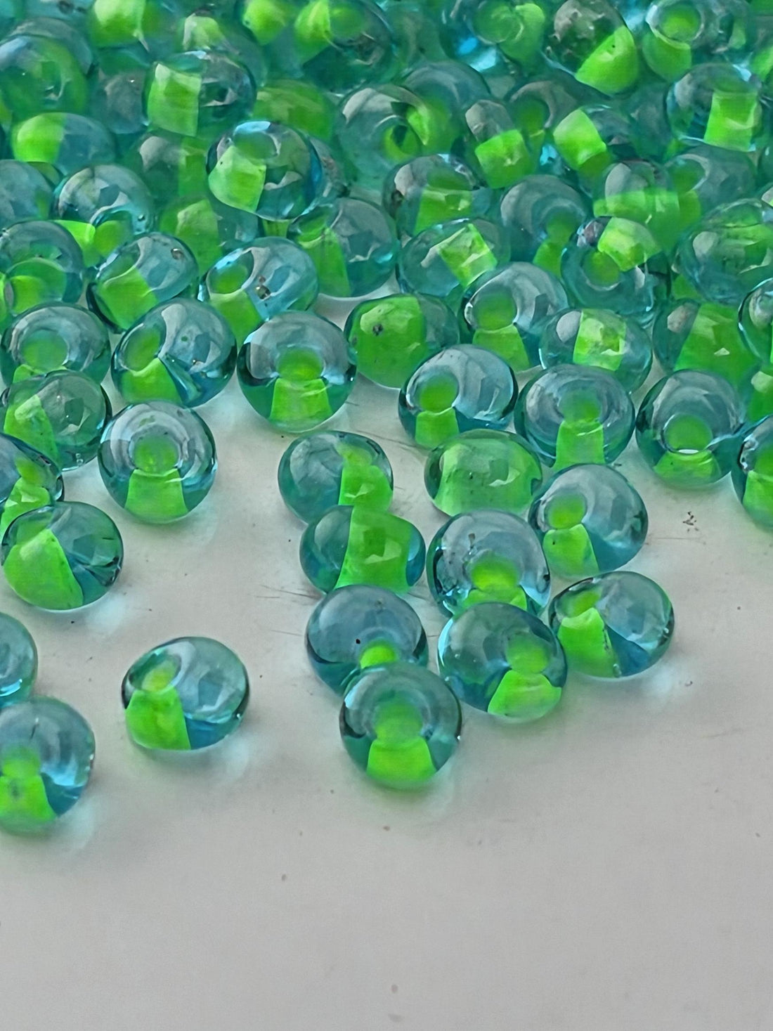 a close-up view of numerous small, clear glass beads scattered across a dark background. The beads have a green tint, creating a visually striking contrast against the dark backdrop.